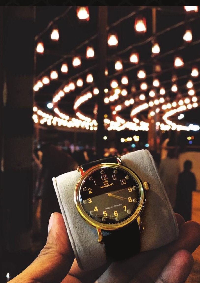 A gold Makkah watch held in the hand beneath the chandeliers of the Haram